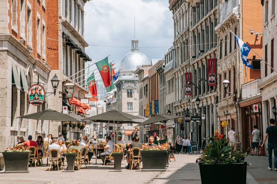 Uma rua movimentada com cafés ao ar livre, edifícios históricos e bandeiras.