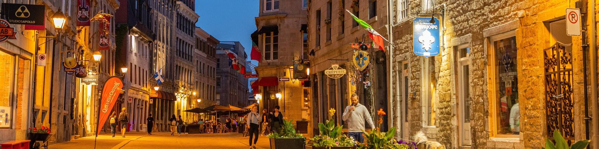 A cobblestone street lined with historic buildings, outdoor seating, and potted plants.