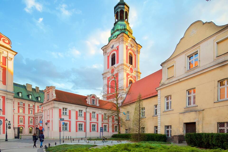 Uma praça histórica com uma torre de igreja imponente, edifícios clássicos e um jardim bem cuidado.