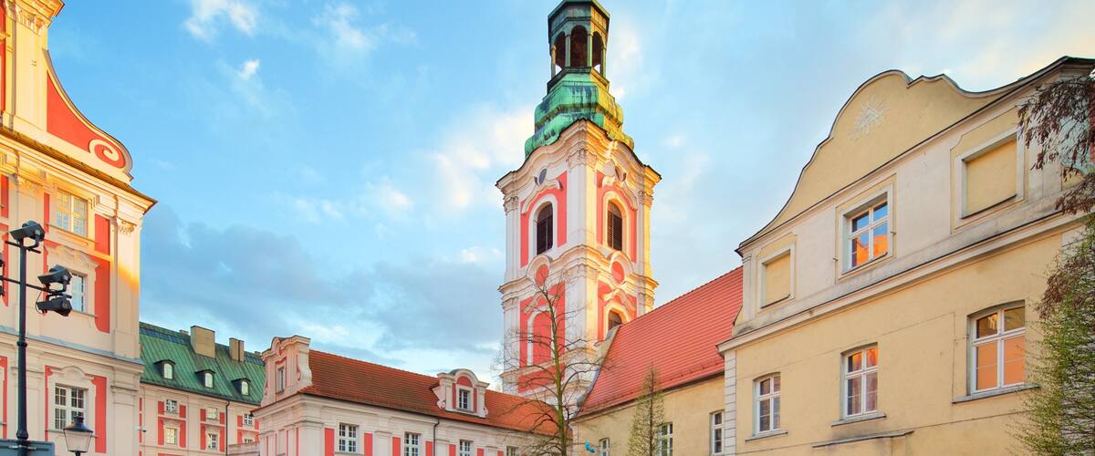 A historic square with a prominent church tower, classical buildings, and a well-maintained garden.
