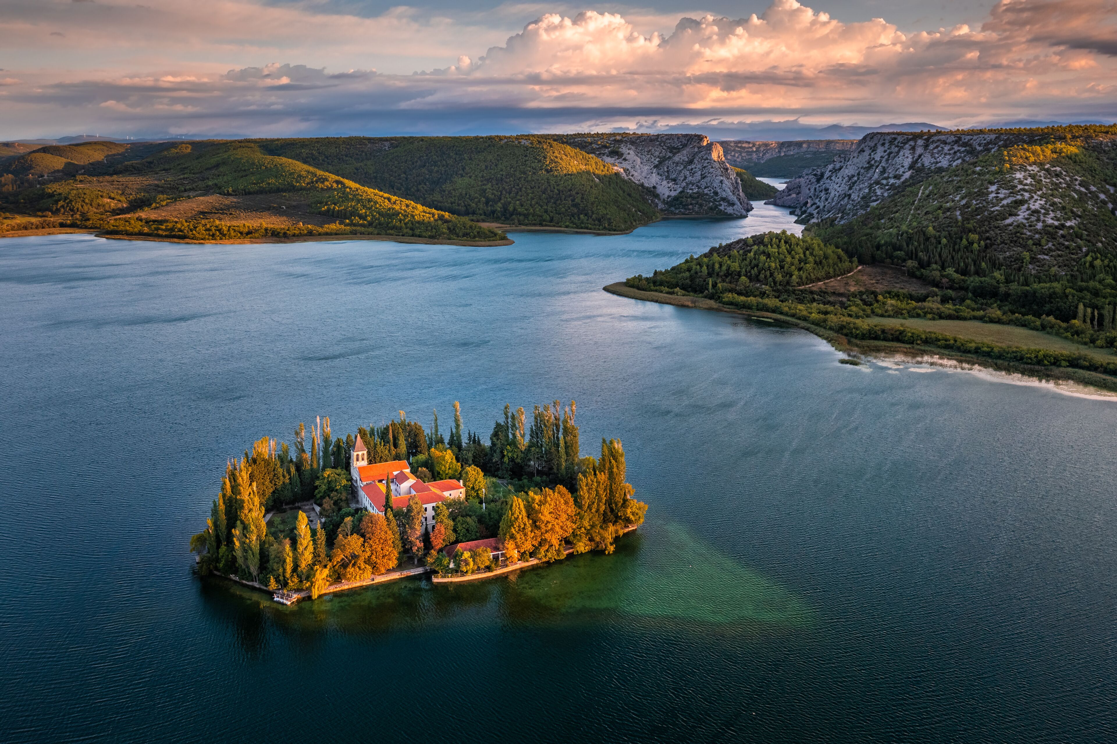 A lake surrounded by hills, a small island with a church, and a distant mountain range.