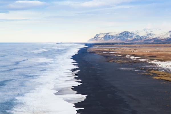 Reynisfjara black sand beach view from Dyrholaey, the 'door-hole', in Iceland at sunset with view of near glacier mountains