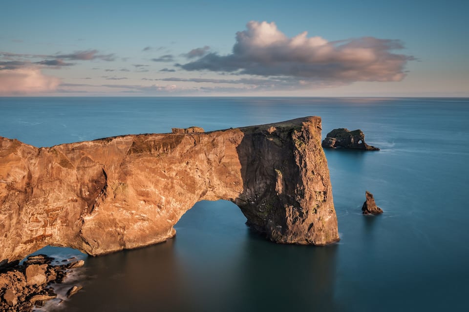 Un gran arco rocoso sobre aguas tranquilas, con un cielo despejado y formaciones rocosas en la distancia.