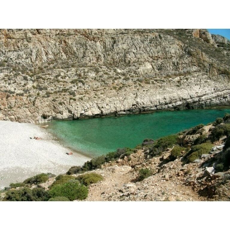 Litoral rochoso com mar azul-turquesa límpido e uma praia de areia.