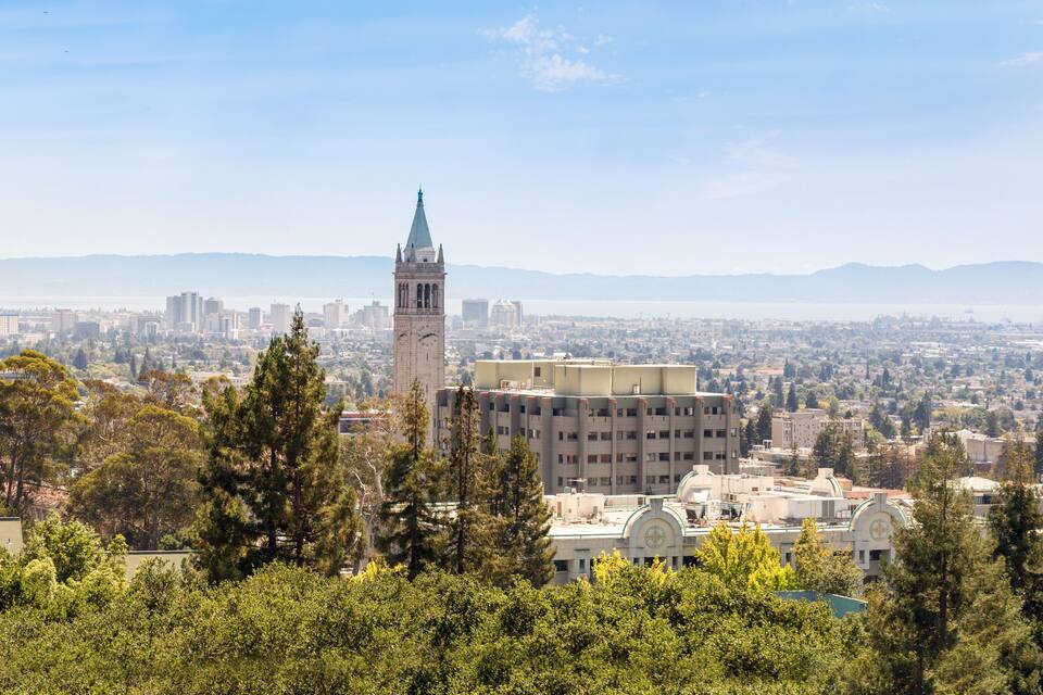 A cityscape with a prominent clock tower, dense urban buildings, and a distant body of water.