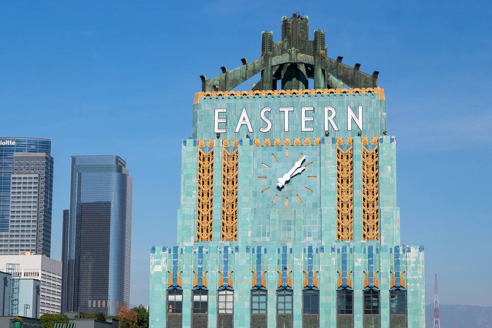 Un reloj de torre con la palabra 'EASTERN' escrita, rodeado de modernos rascacielos.