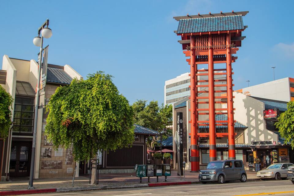 A traditional red pagoda, a modern building, and a street with cars and trees.