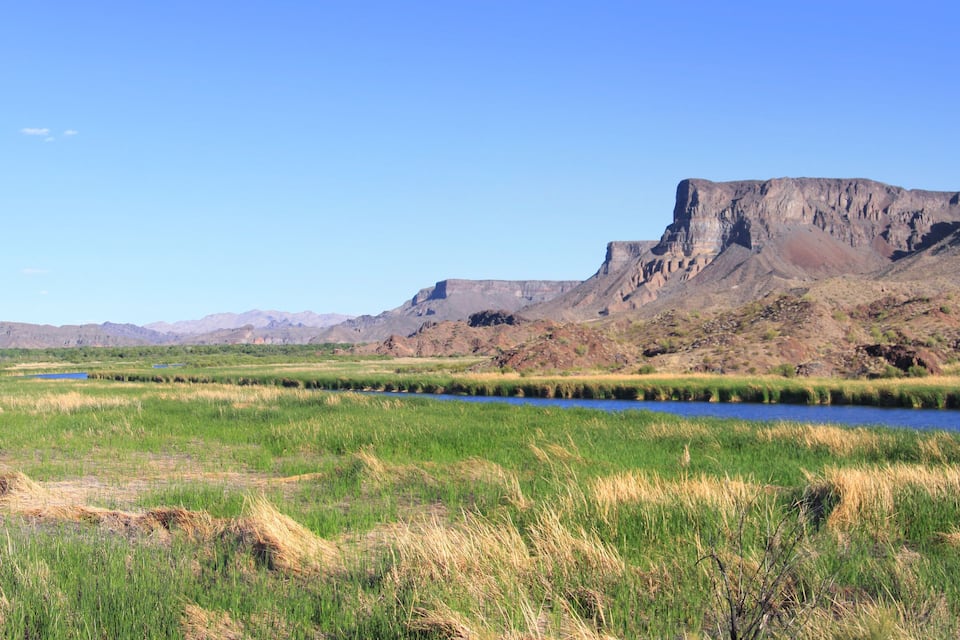 A river meandering through a grassy valley with a prominent rocky cliff in the background.