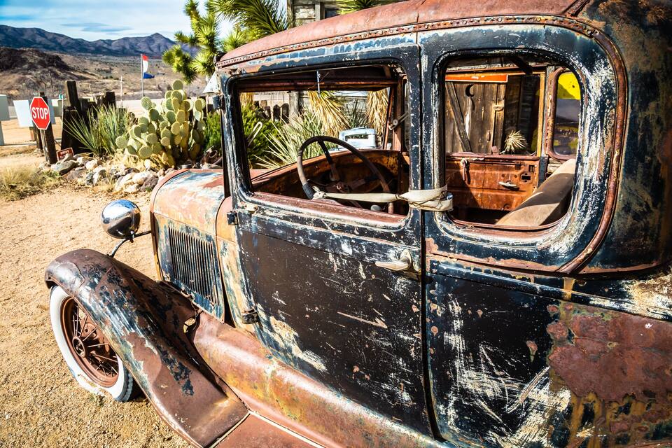 Un coche antiguo y oxidado de época, con una señal de stop y cactus al fondo.