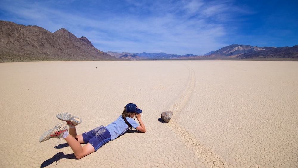 A person lying on a cracked desert surface with mountains in the background.