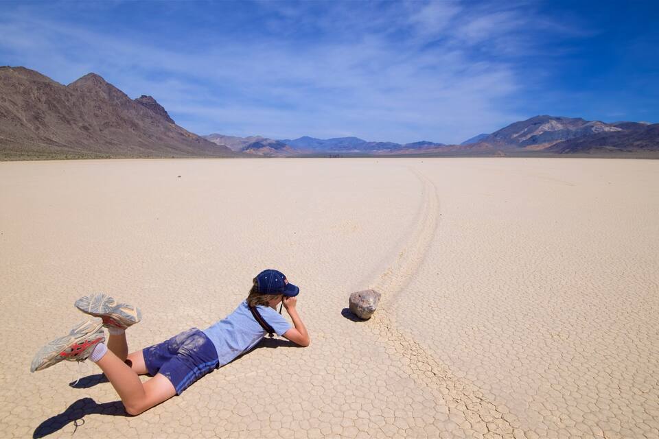 A person lying on a cracked desert surface with mountains in the background.