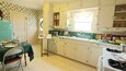 A vintage kitchen with a teal table, a white refrigerator, and a window with curtains.