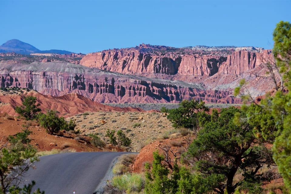 A winding road through a desert landscape with red rock formations and sparse vegetation.