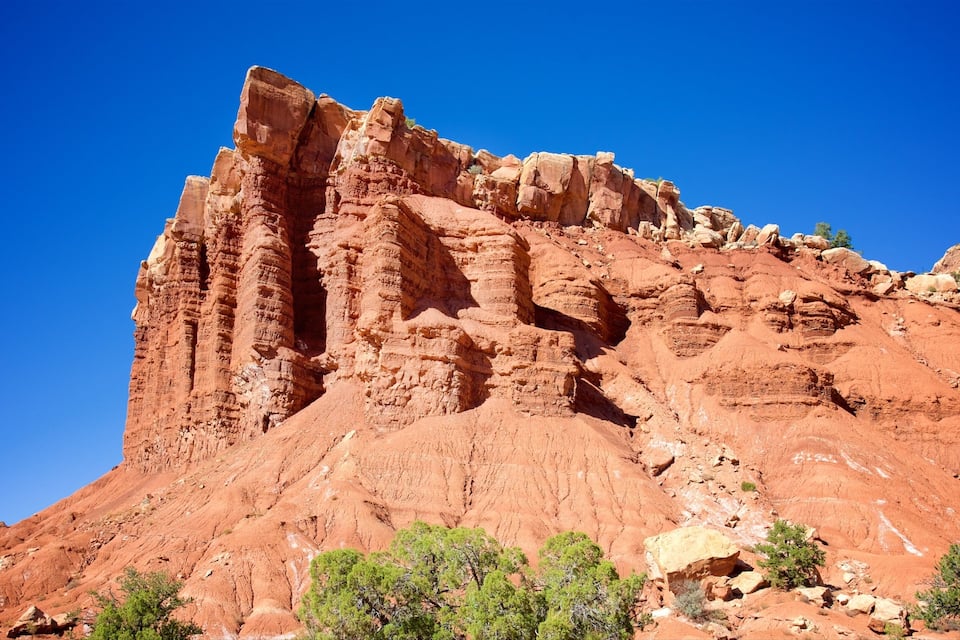 A red rock formation with layered cliffs and sparse vegetation.