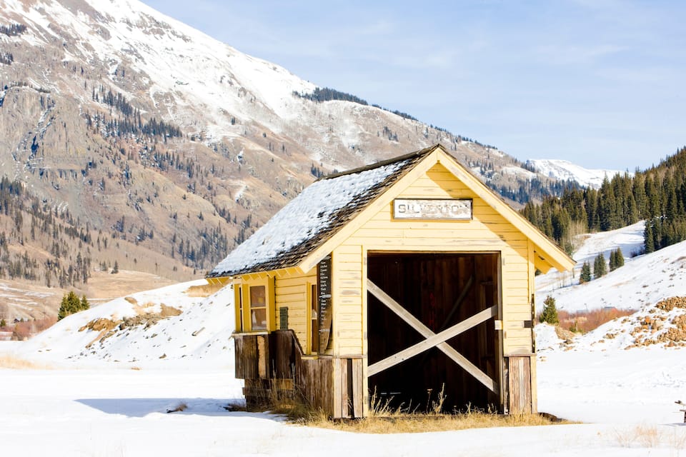 Una cabaña de madera con un letrero que dice "SILVERTON" en una zona montañosa nevada.