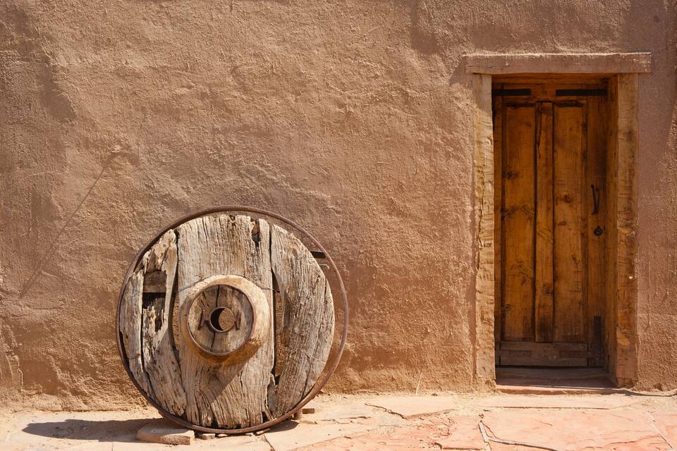 Uma porta de madeira rústica e um barril de madeira desgastado, tudo em frente a uma parede texturizada.