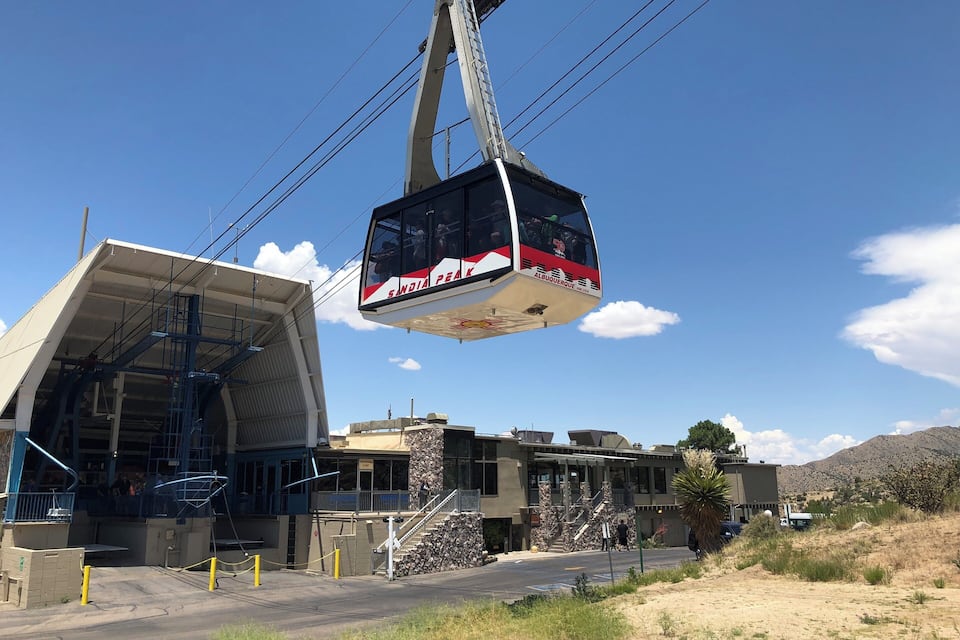 A cable car at a station with a modern building and a mountainous backdrop.
