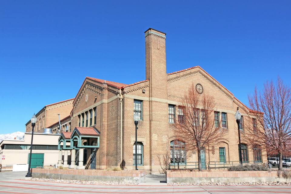 A historic brick building with a clock tower, large windows, and a green entrance.