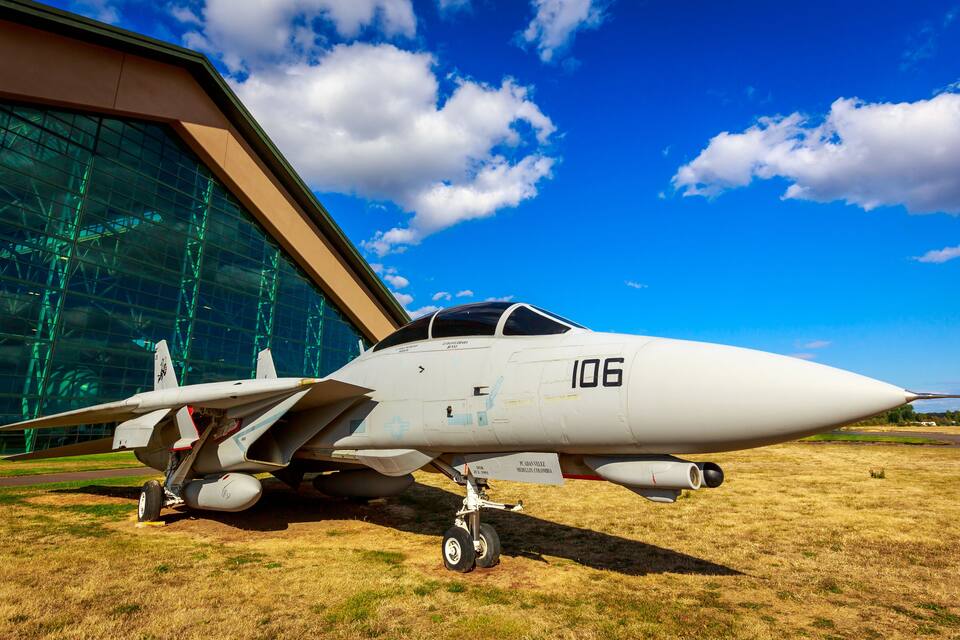 A fighter jet with the number 106 parked in front of a modern building with large glass windows.