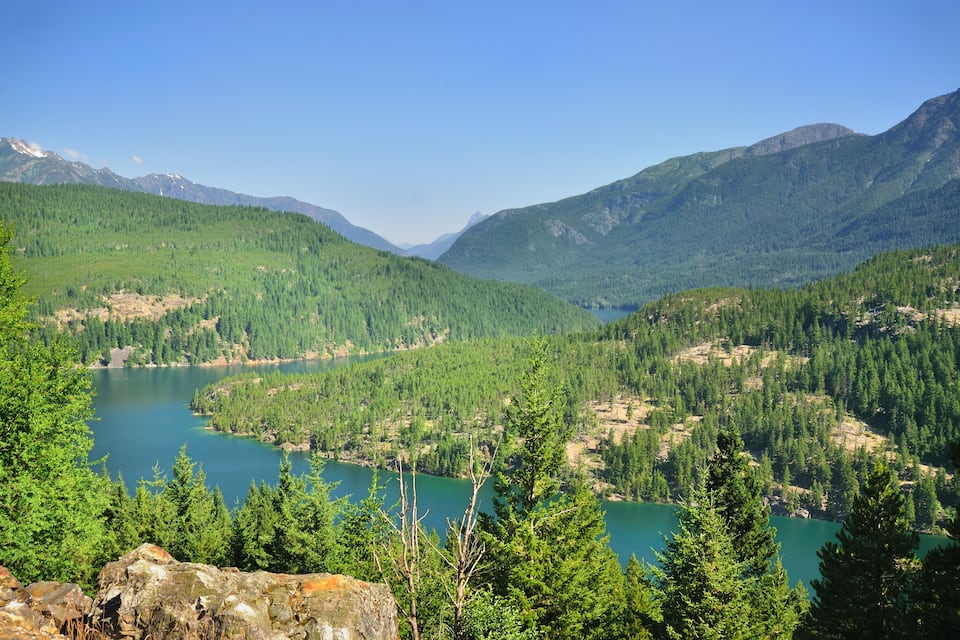 A mountainous landscape with a lake surrounded by dense forests and rocky terrain.