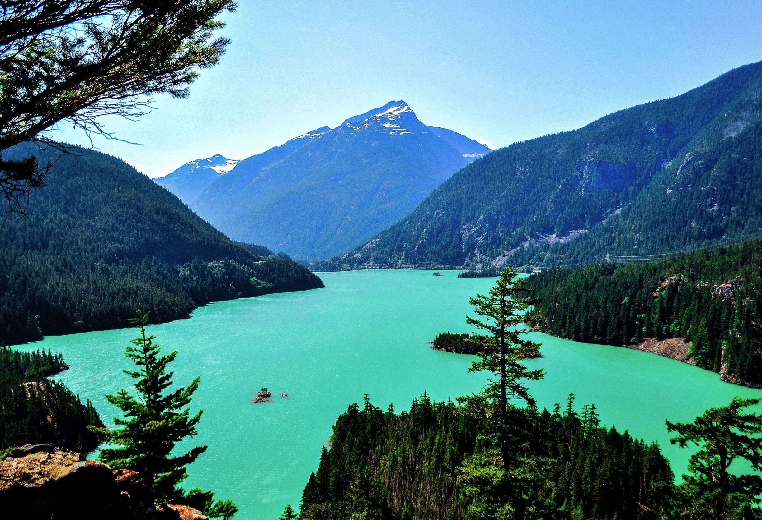 A turquoise lake surrounded by dense forests and a snow-capped mountain.