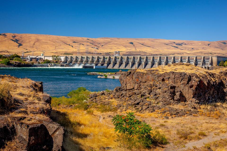 A dam with a river flowing through it, surrounded by dry hills.