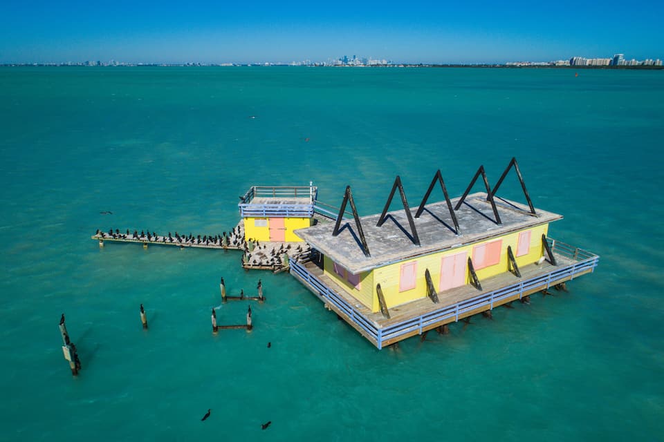 Un muelle colorido que se adentra en aguas turquesas, con un horizonte urbano a lo lejos.