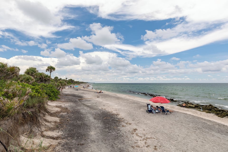 Une plage avec un parasol rouge, un rivage rocheux et des palmiers.