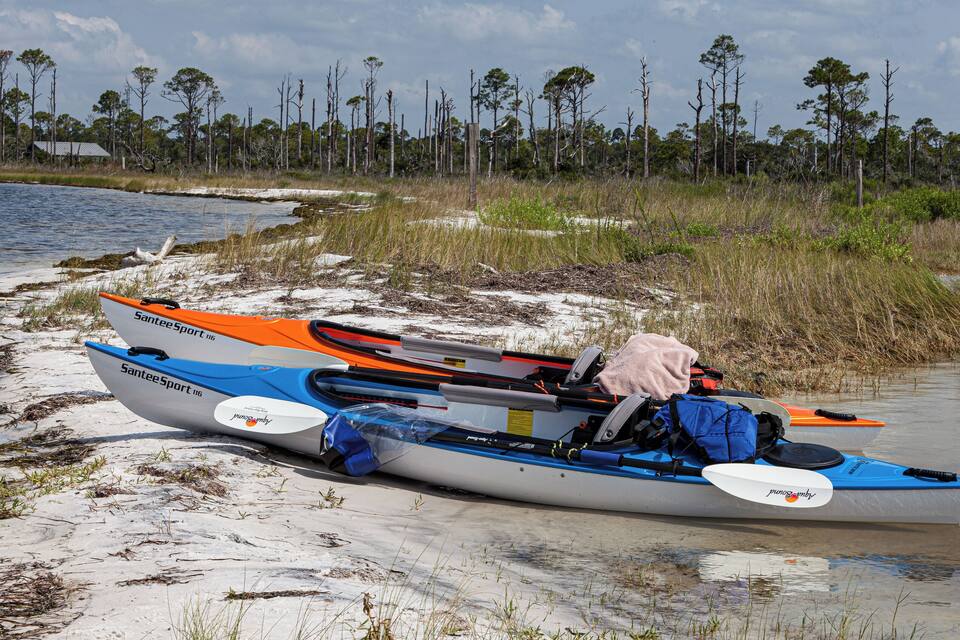 A kayak with a towel and gear on a sandy beach near water.