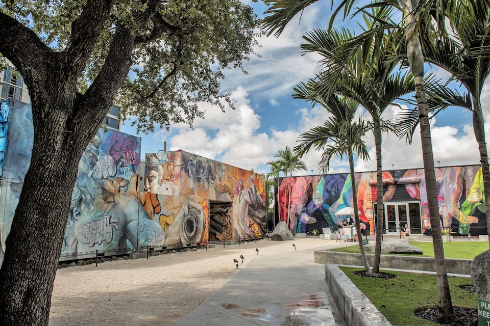 Un edificio cubierto de murales, un sendero y palmeras.