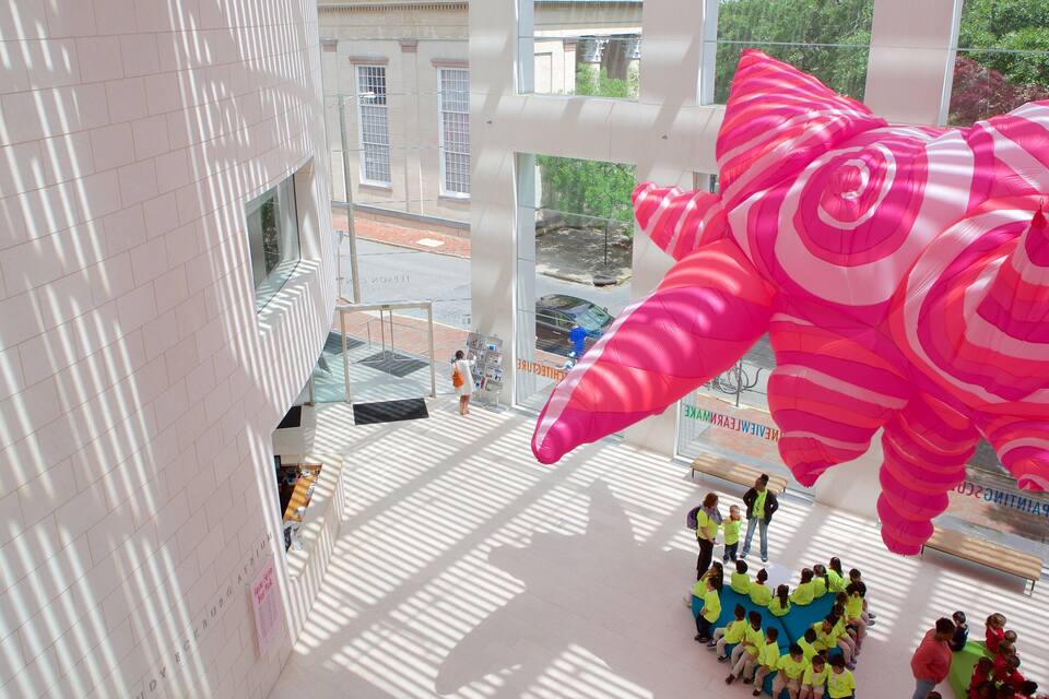 A large pink balloon sculpture in an indoor space with a group of children and adults gathered below.