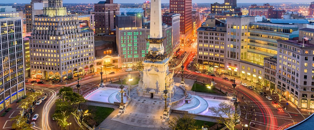 A cityscape with a prominent monument in the center, surrounded by modern buildings and a busy intersection.