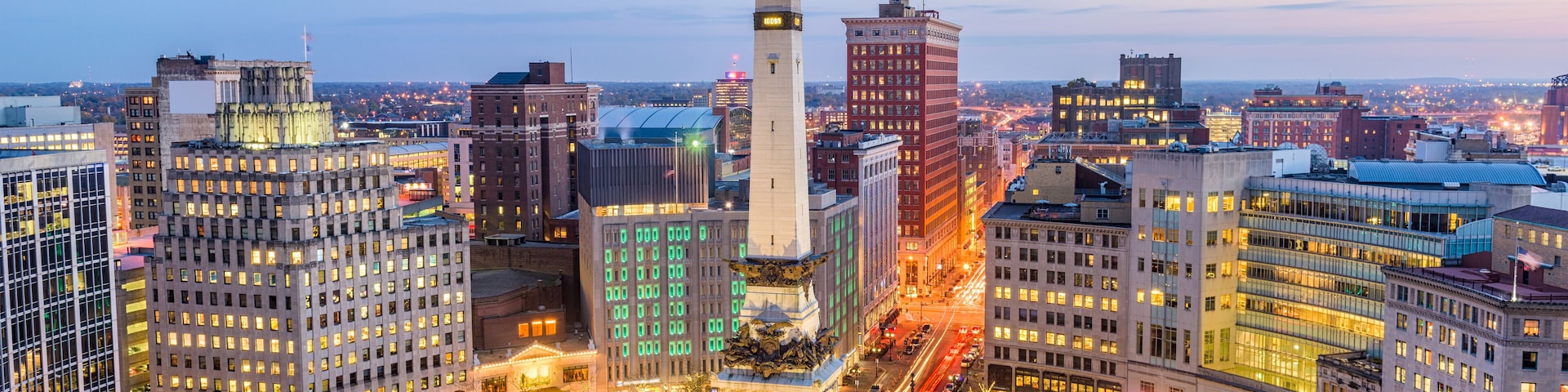 A cityscape with a prominent monument in the center, surrounded by modern buildings and a busy intersection.