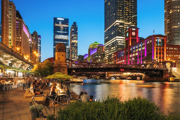 Une vue nocturne d’une ville, avec des bâtiments illuminés, une rivière et un pont.
