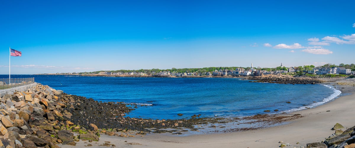 A coastal town with a sandy beach, rocky shoreline, and a prominent American flag.
