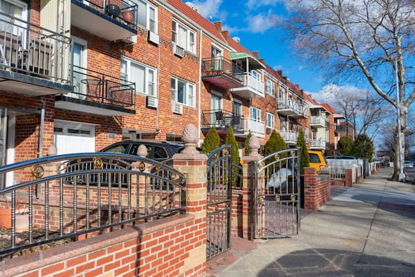 A row of red brick townhouses with balconies, a gated driveway, and a yellow van parked on the street.