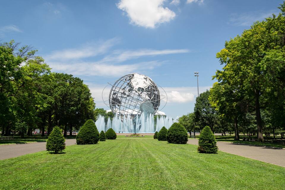 Un parque con una gran escultura de un globo terráqueo, rodeado de árboles y una fuente.