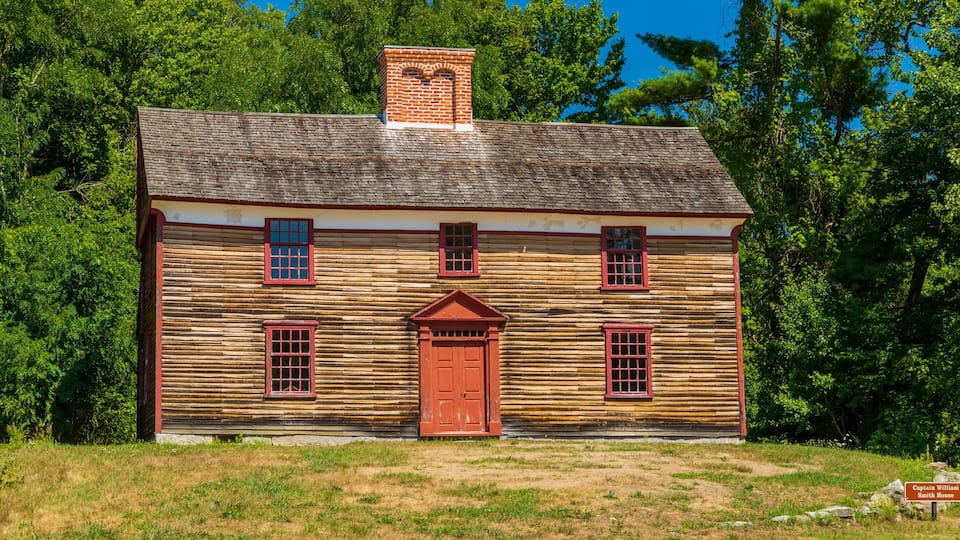 A wooden log cabin with a red door and windows, surrounded by trees.