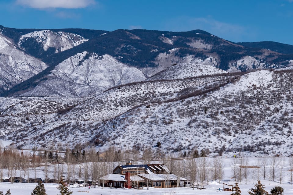 A snow-covered mountain range with a lodge and a ski slope in the foreground.