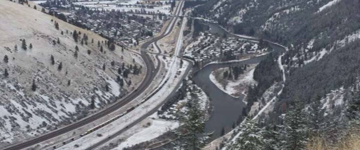 A snow-covered valley with a winding river, a highway, and mountains in the background.