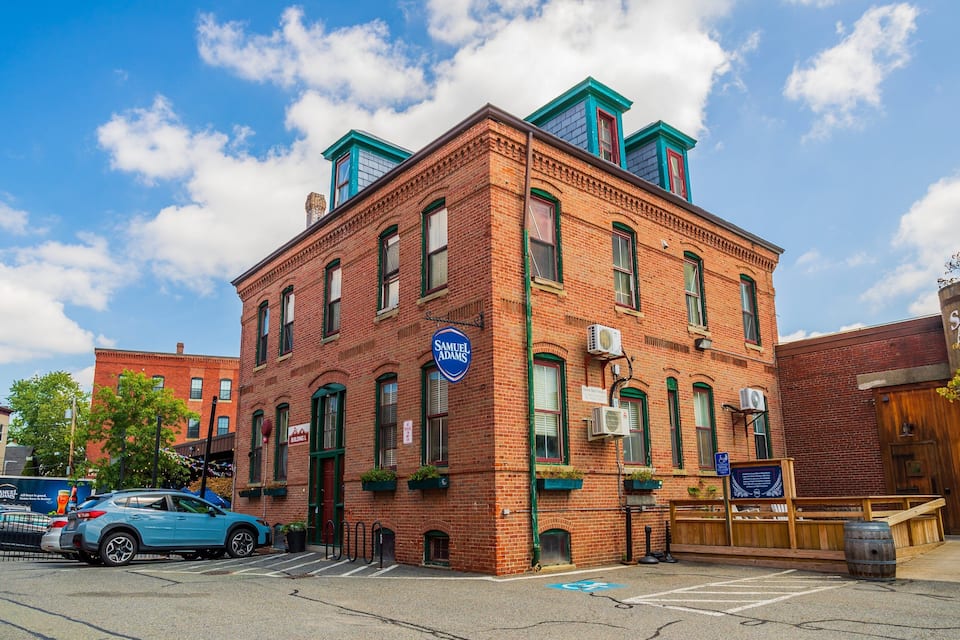 A red brick building with green trim and a blue sign reading "Samuel Adams."
