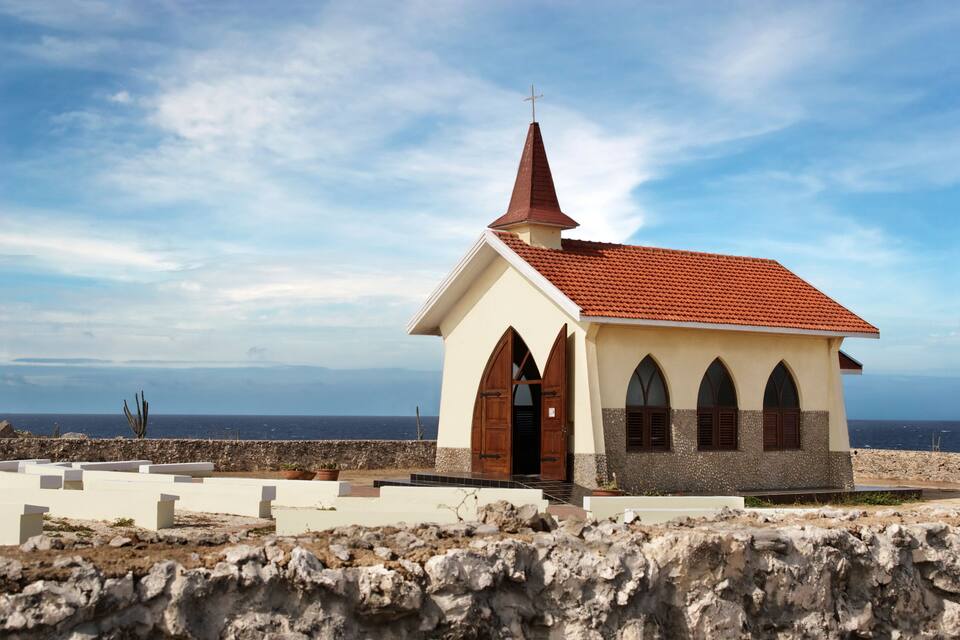 Eine kleine Kirche mit rotem Dach und Kruzifix, in der Nähe einer felsigen Küstenlinie gelegen.