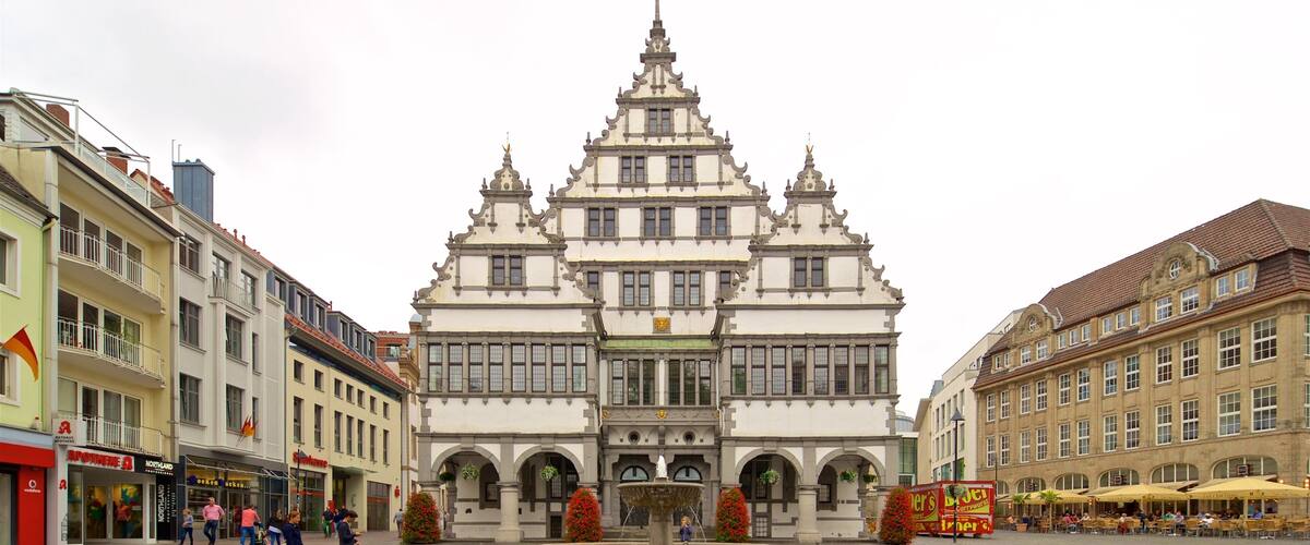A historic building with ornate architecture, a central fountain, and surrounding shops and cafes.