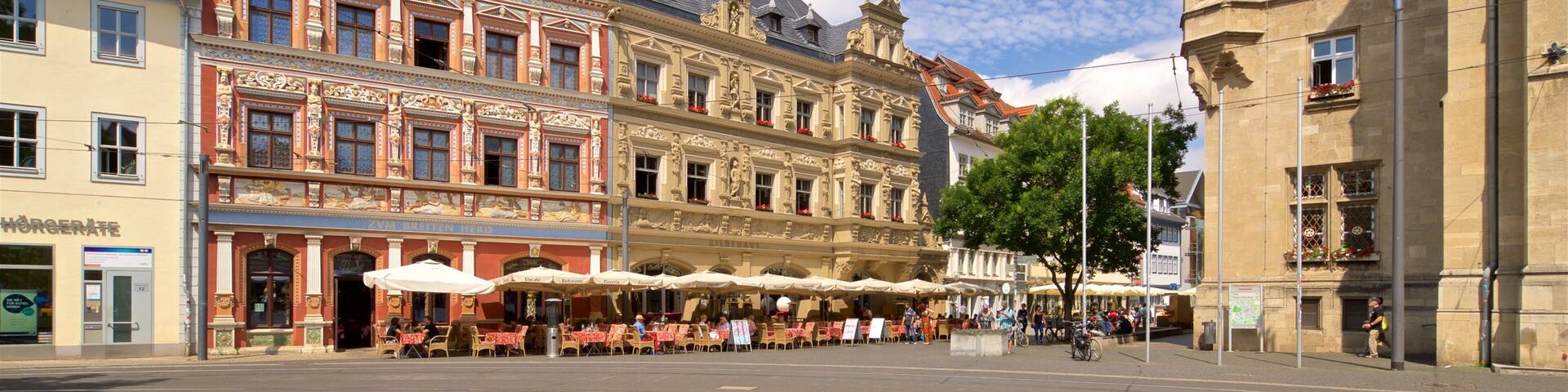 A historic European street with ornate buildings, outdoor cafes, and a clear blue sky.