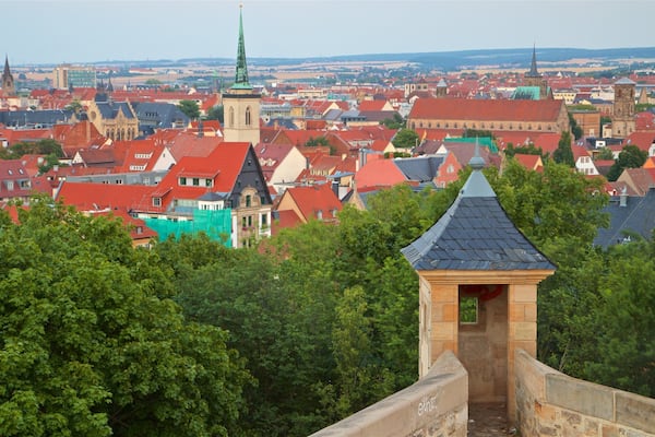 A cityscape with red-roofed buildings, a prominent church tower, and lush green trees.