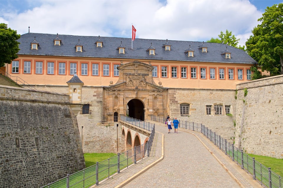 Un bâtiment historique doté d’un mur en pierre, d’un chemin pavé et d’un drapeau rouge.