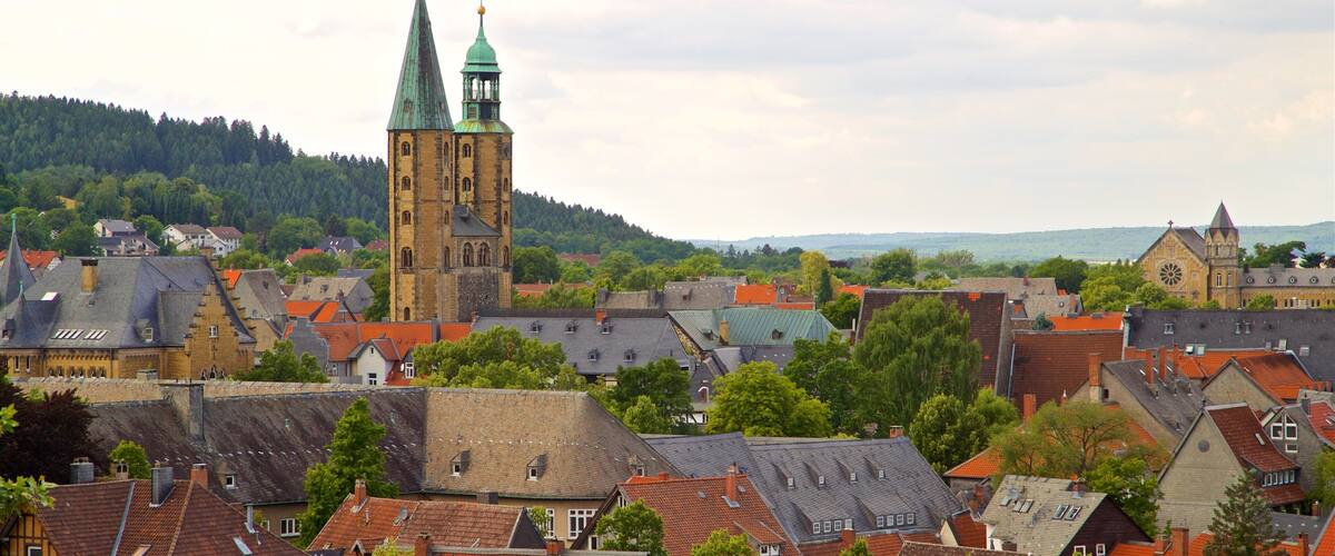 A town with historic buildings, a prominent church with a green spire, and a forested hill in the background.