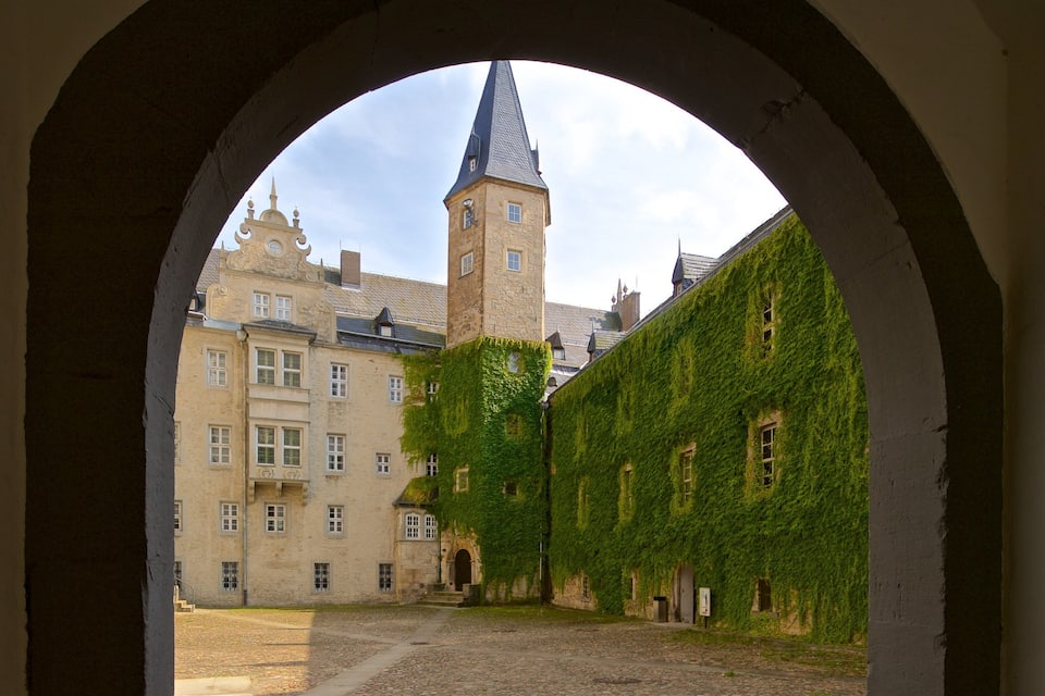 En valvformad öppning som inramar en innergård med ett torn och byggnader täckta av murgröna.