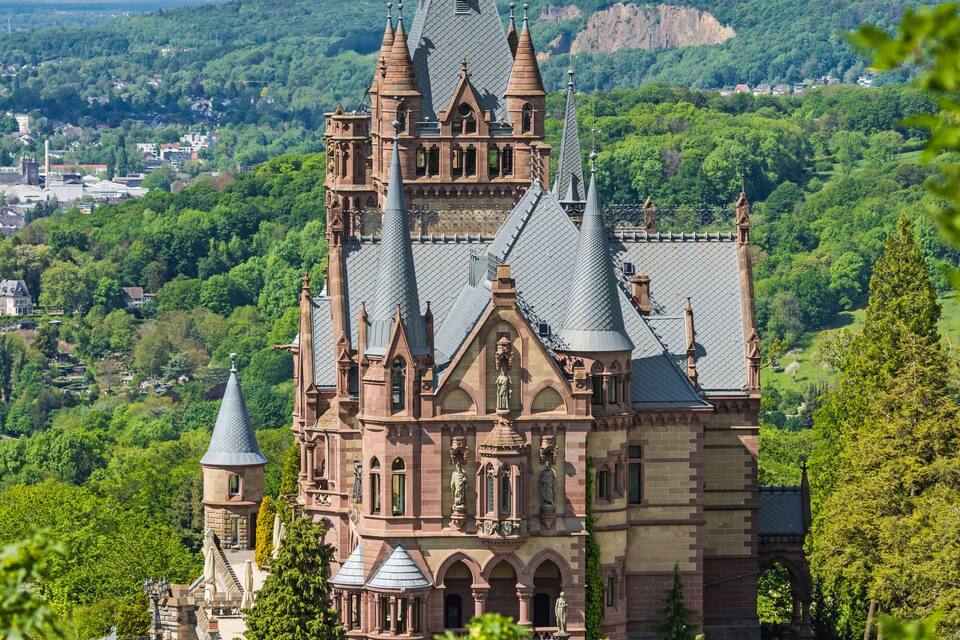 A historic church with multiple spires, surrounded by lush greenery and a mountainous backdrop.