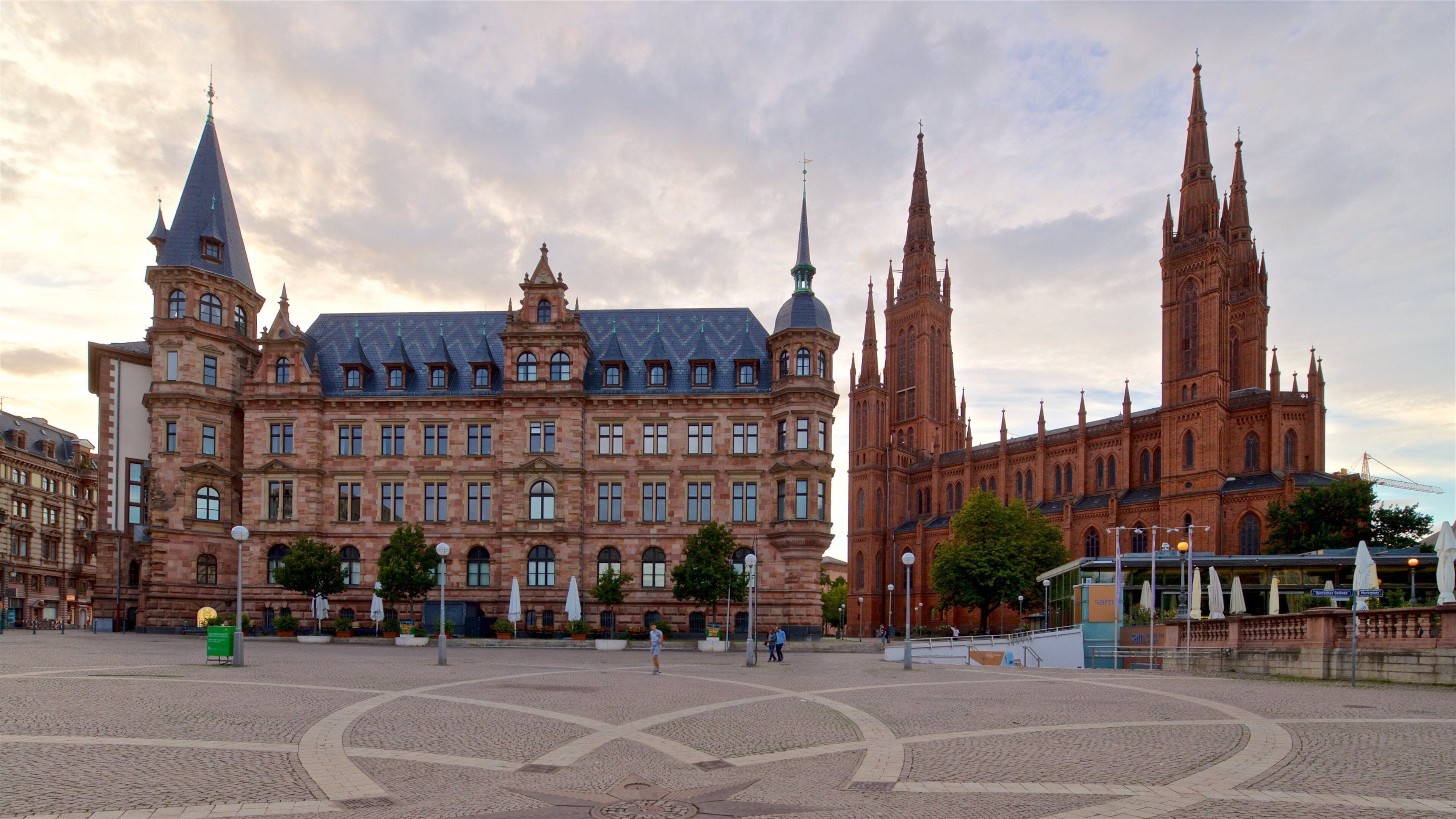 A historic building with multiple spires and a large central tower, surrounded by a cobblestone plaza.